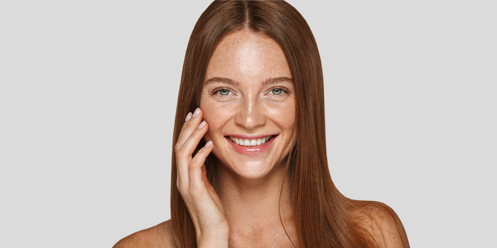 Headshot of a smiling red haired woman, her hand resting on her cheek.